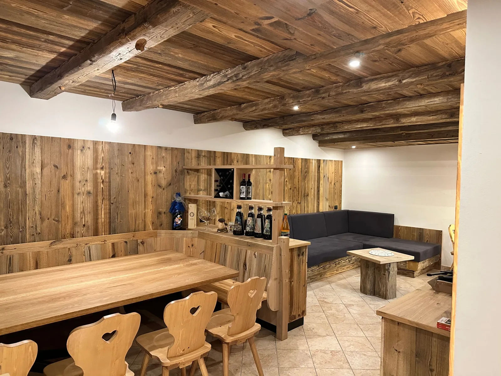 Stube mit Balkendecke aus dunklem Holz, Eckbank mit Herzlehnenstühlen, langer Holztisch und Weinregal