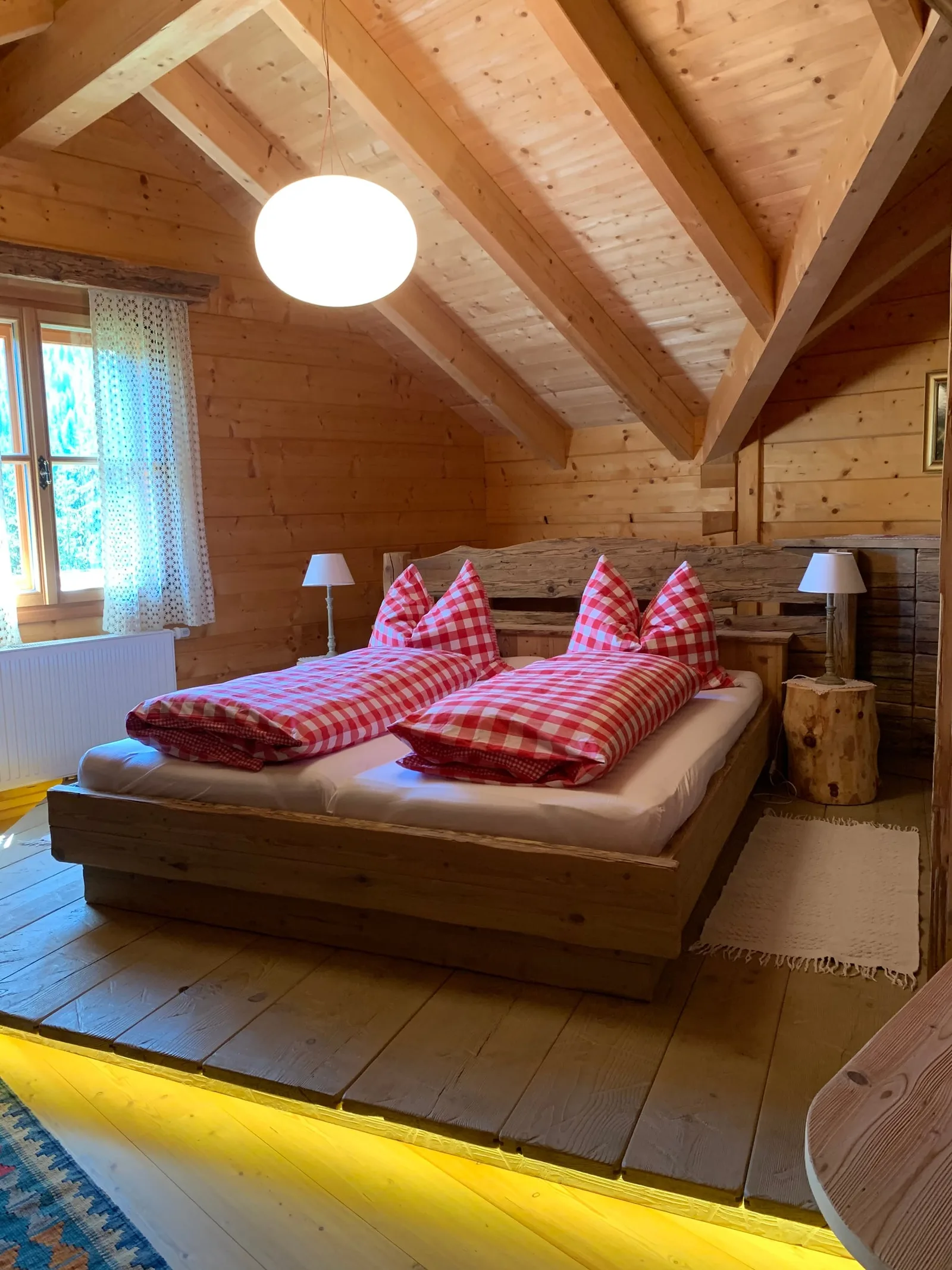Schlafzimmer unter dem Dach mit Holzbett auf einem Podest und rot karierter Bettwäsche