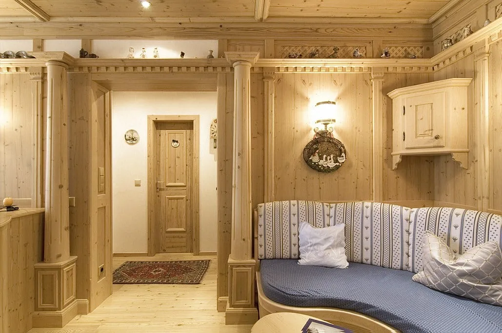 Stube aus hellem Holz mit Säulen, Wandschrank und Eckbank