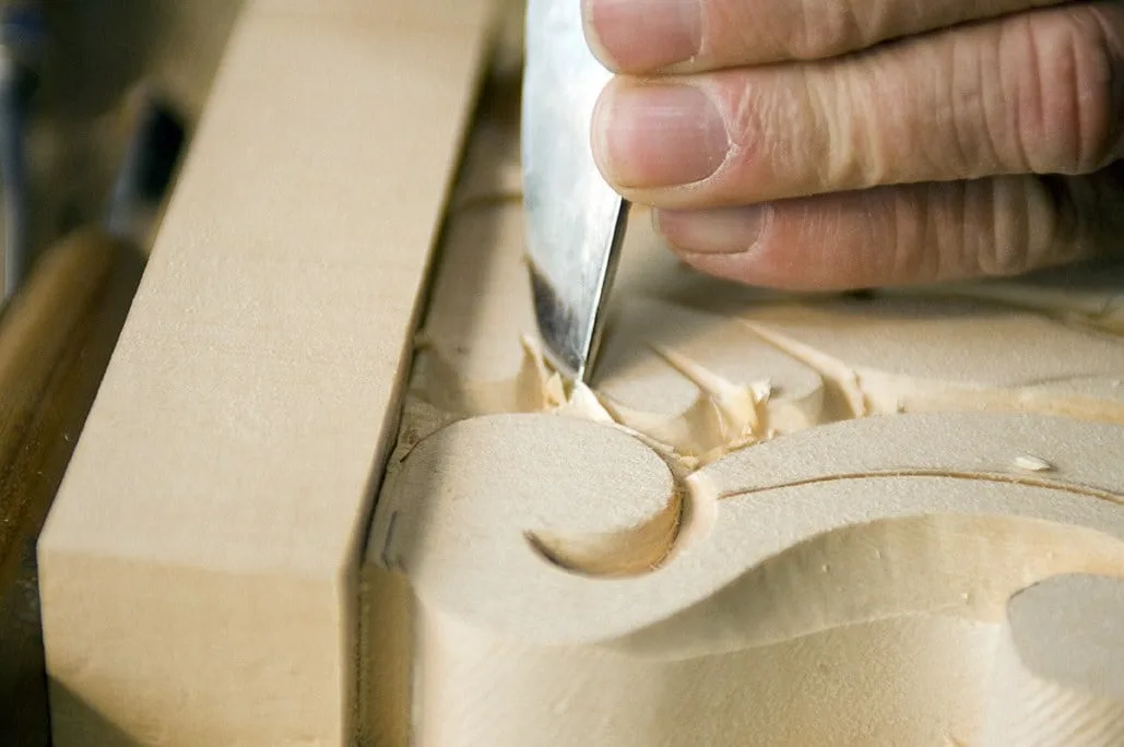 Hand mit Schnitzeisen an einer geschwungenen Volute aus hellem Holz