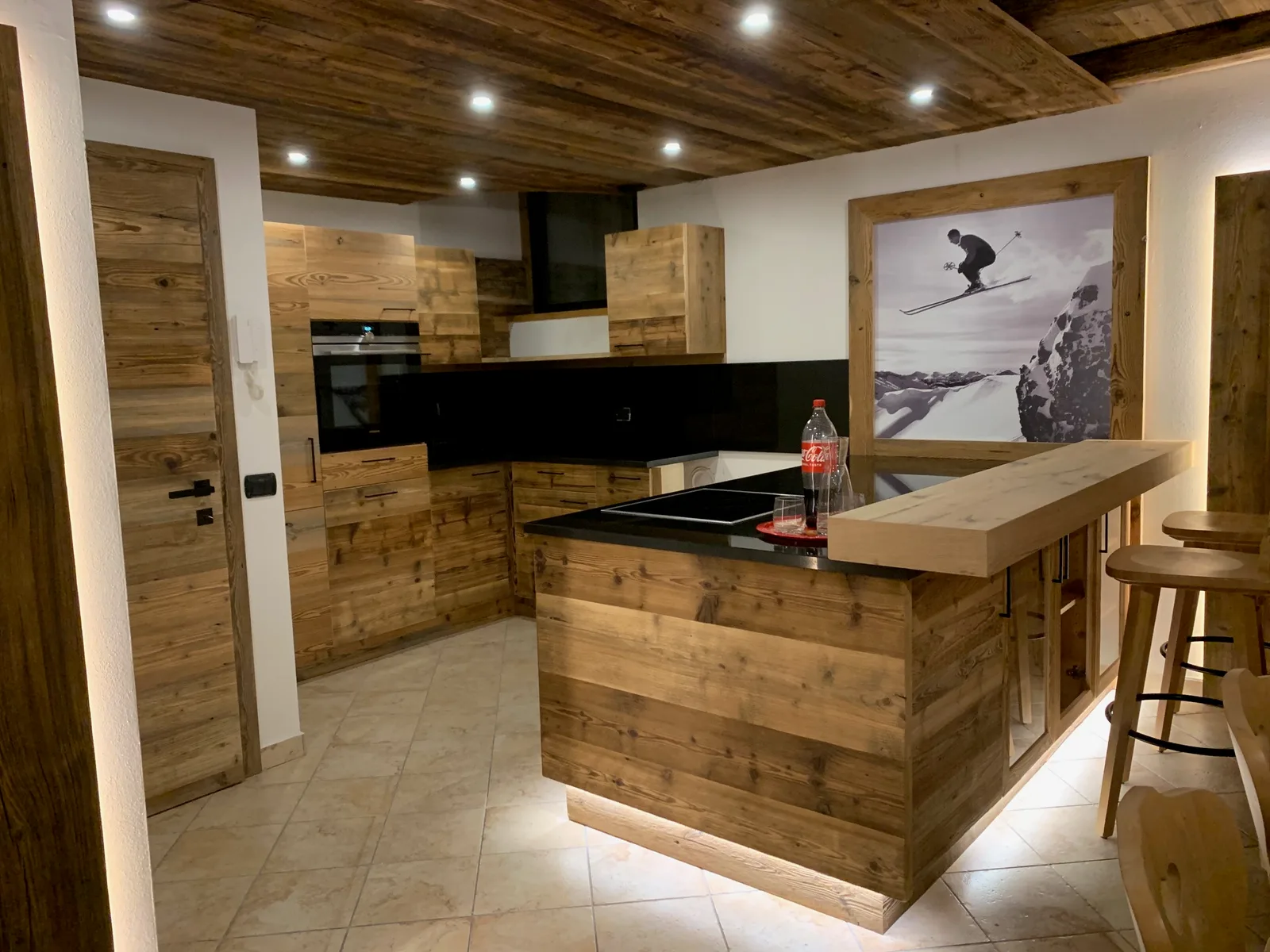 Küche mit Fronten aus dunklem Holz, Theke mit Barhockern und Holzdecke